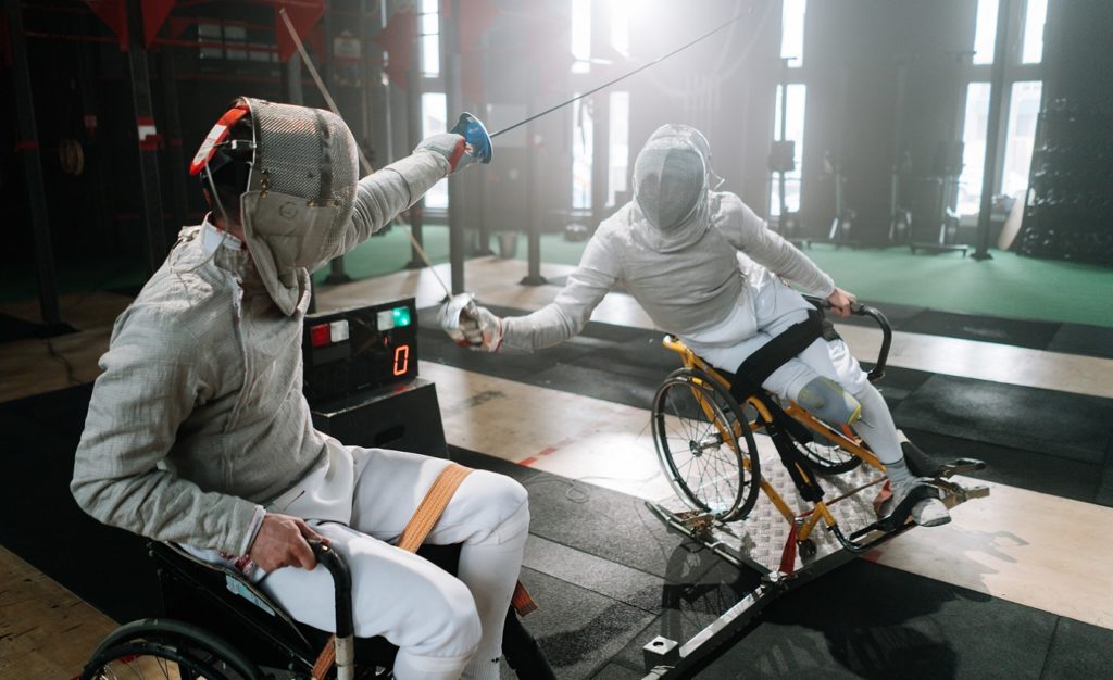 Zwei Personen mit Bewegungsstörungen im Rollstuhl sitzend am Fechten.