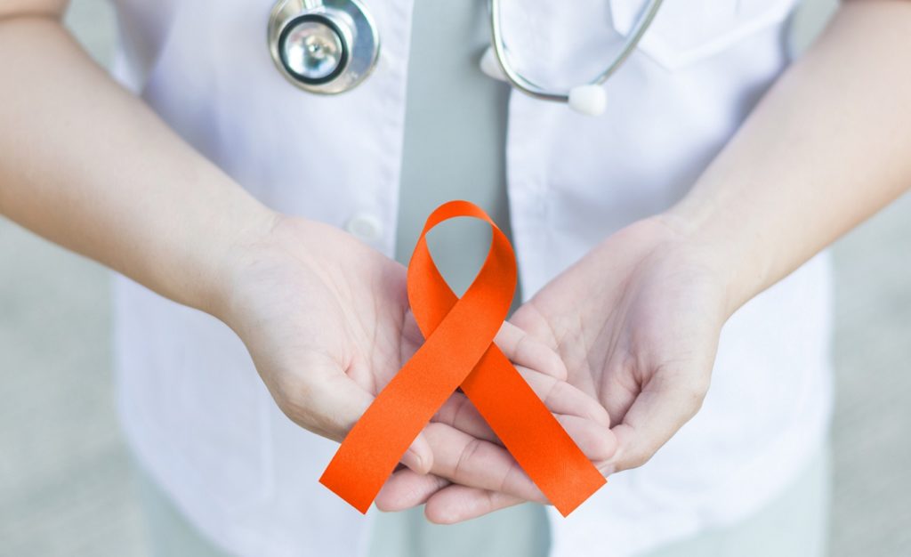 Eine Ärztin in weißer Uniform hält ein orange gefärbtes Band, das als Symbol für die Unterstützung von Menschen mit Multipler Sklerose (MS) dient.