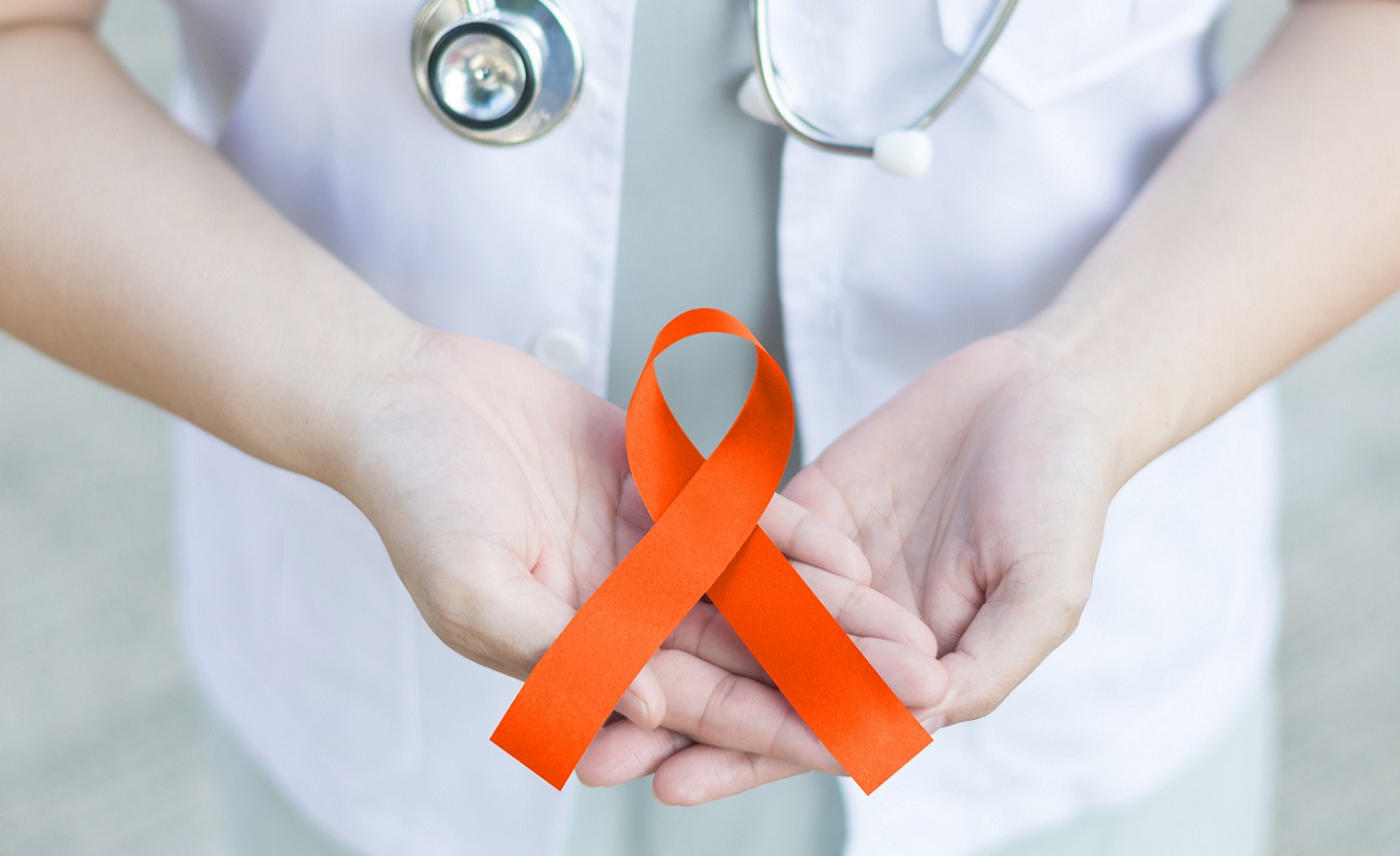 Eine Ärztin in weißer Uniform hält ein orange gefärbtes Band, das als Symbol für die Unterstützung von Menschen mit Multipler Sklerose (MS) dient.