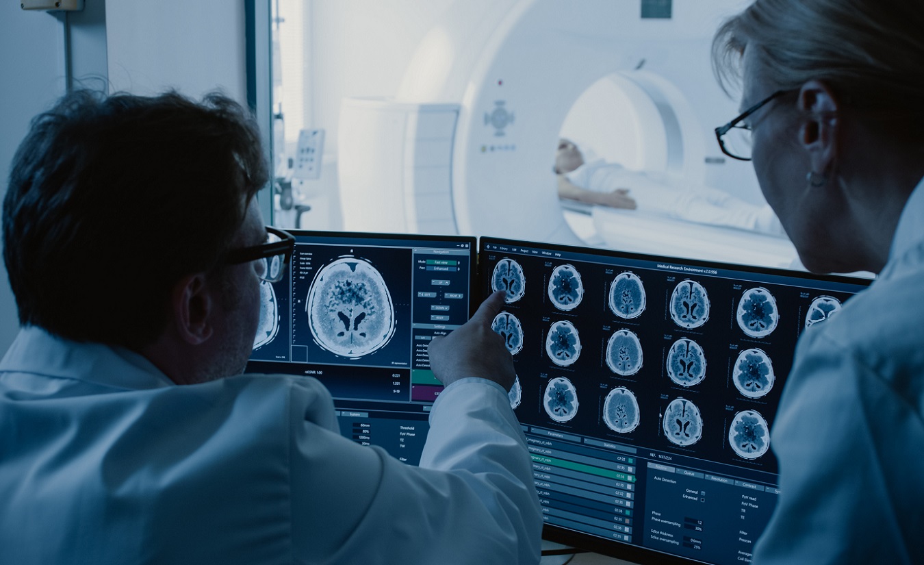 Zwei medizinische Fachkräfte, ein Arzt und ein Radiologe, analysieren und diskutieren eine Magnetresonanztomographie (MRT)-Diagnose im Kontrollraum.