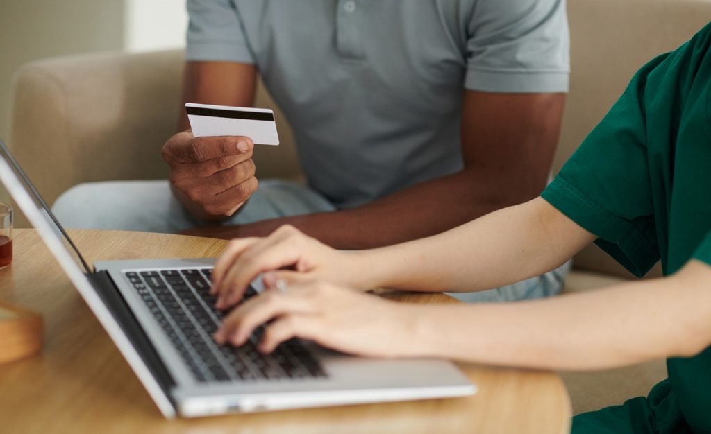 Eine fürsorgliche Begleitperson hilft einer Person mit Multipler Sklerose (MS) dabei, online einen Antrag für einen Schwerbehindertenausweis auszufüllen. Gemeinsam sitzen sie an einem Tisch, während die Person mit MS ihr Tablet bedient. Die Begleitperson steht zur Seite und bietet Hilfe und Ermutigung.