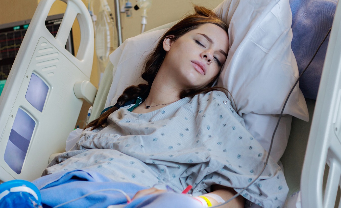 Eine erschöpfte junge Frau mit Multipler Sklerose liegt im Krankenbett und erhält einen Kortison-Tropf.