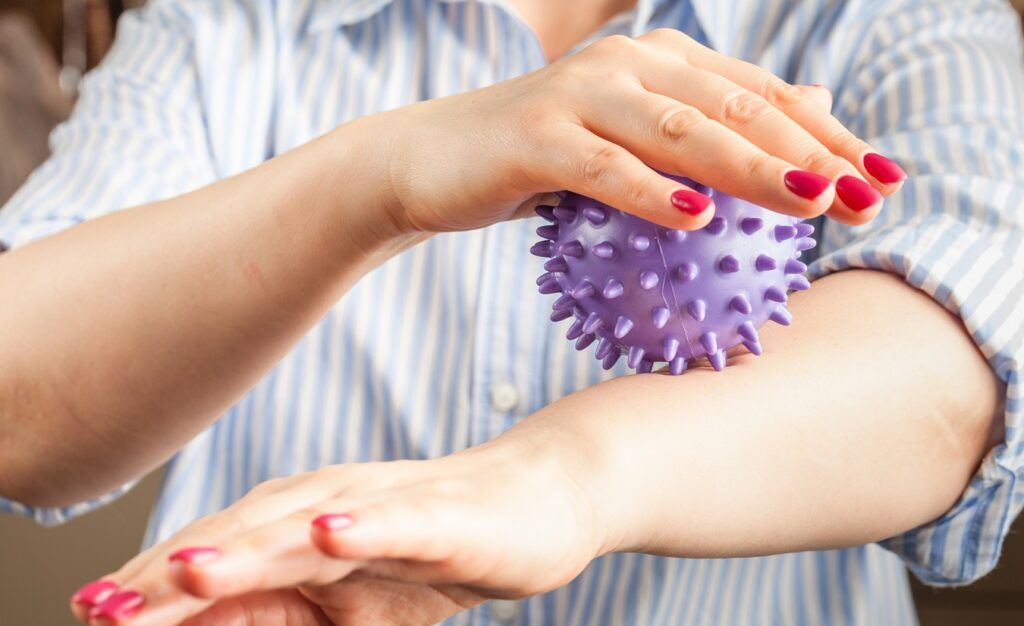 Frau mit Multipler Sklerose sitzt entspannt auf einer Massageliege und erhält Ergotherapie mit einem Igelball zur Linderung von Sensibilitätsstörungen.