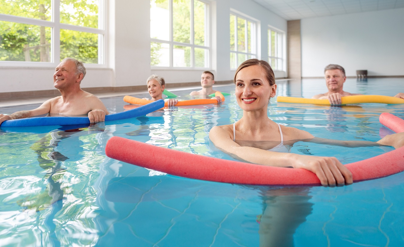 Eine Gruppe von Patienten mit Multipler Sklerose (MS) nimmt an Wassergymnastik-Übungen in einem Hallenbad teil.