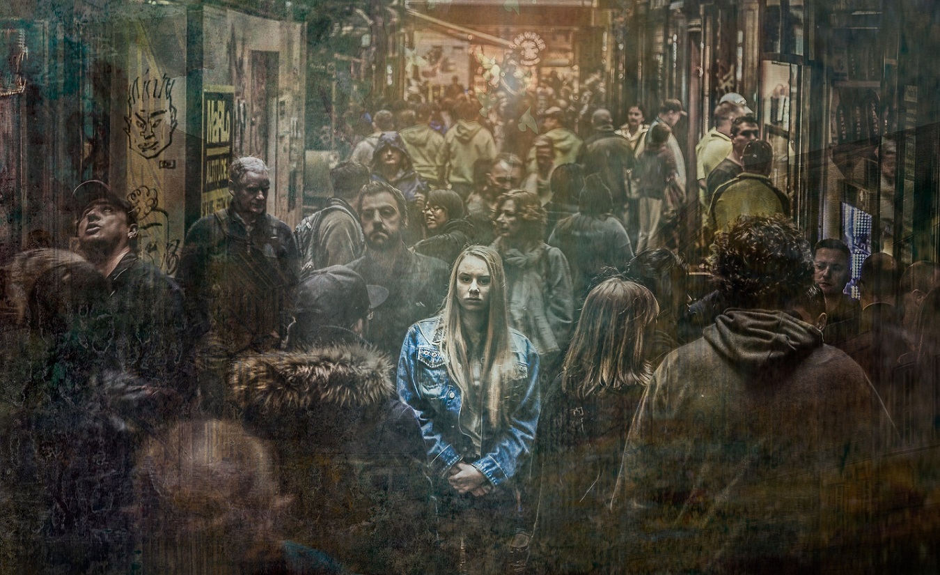 Ein farbiges Porträt einer jungen Frau inmitten einer schwarz-weißen Menschenmenge. Die Frau mit blonden Haaren und einer blauen Jeansjacke wirkt überfordert und ängstlich, möglicherweise aufgrund einer Angststörung in Verbindung mit oder zusätzlich zur Multiplen Sklerose.