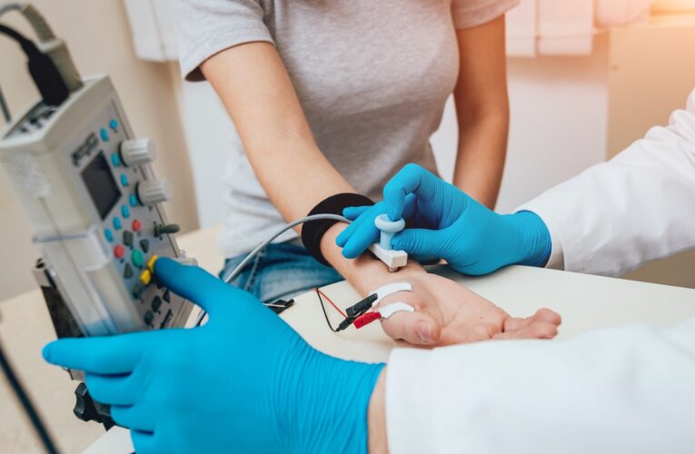 Medizinische Fachangestellte führt einen Nervenleitgeschwindigkeitstest an einer Frau mit MS durch. Elektrische Stimulation am Unterarm und Aufzeichnung der Impulse über Klebeelektroden.
