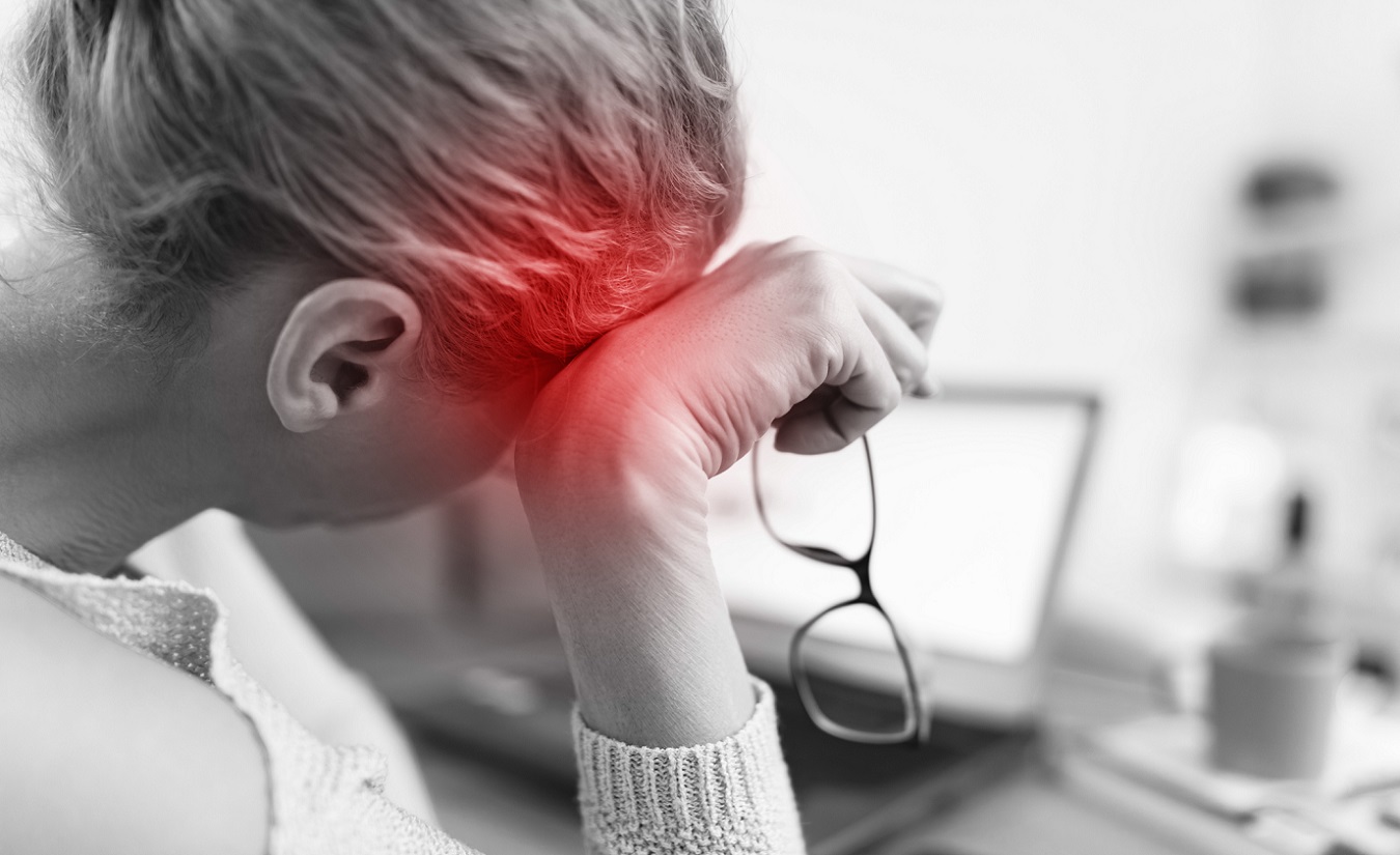 Schwarz-weiß-Bild einer Frau, die am Laptop arbeitet und sich unwohl fühlt. Rötliche Markierungen zeigen ihre Kopfschmerzen an, symbolisierend für MS-bedingte Beschwerden.