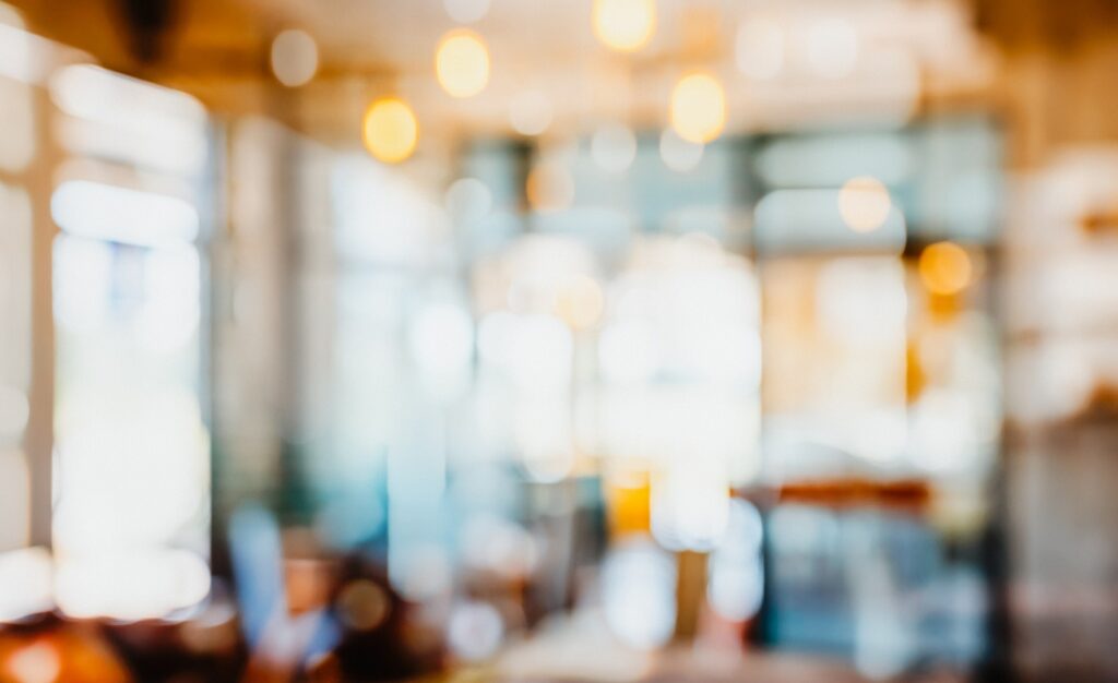 Eine unscharfe Darstellung einer Person, die in einem Café sitzt. Die Umgebung und die Person sind verschwommen und undeutlich erkennbar.