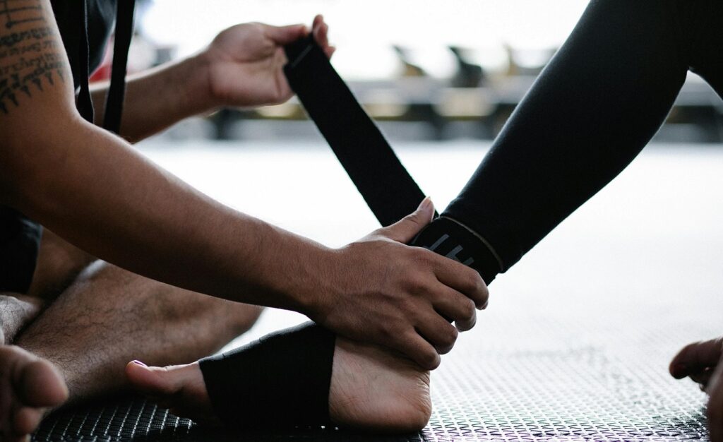 Eine Person sitzt auf dem Boden einer Turnhalle, während eine zweite Person ihr Bein bandagiert.