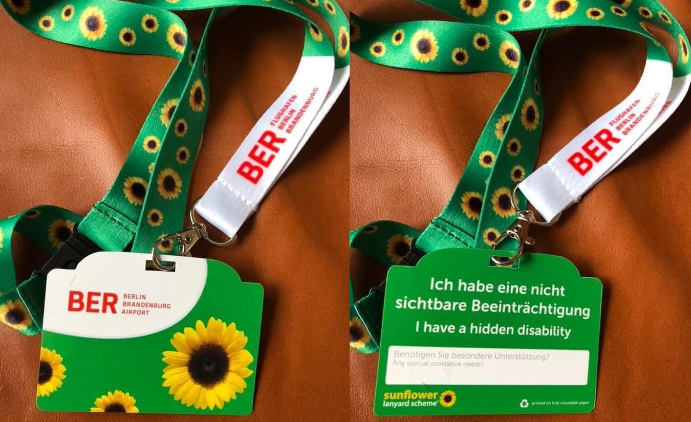 Grünes Umhängeband mit kleinen gelben Sonnenblumen und einer Karte mit der Aufschrift "Ich habe eine nicht sichtbare Beeinträchtigung" und "I have a hidden disability"