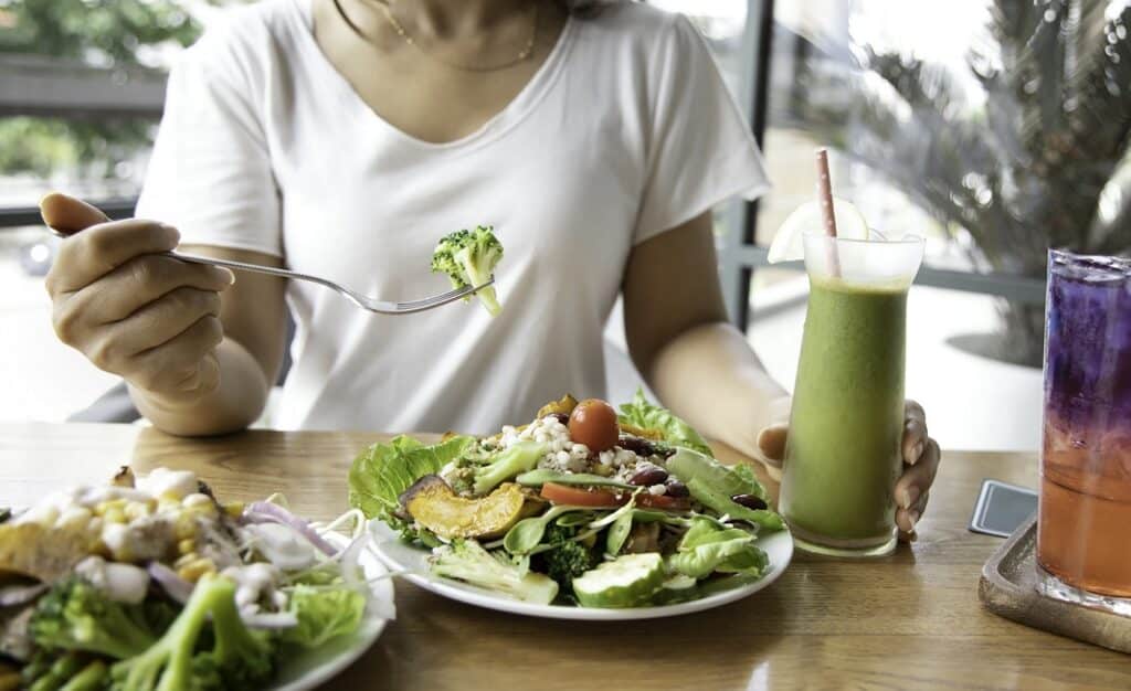 Frau isst gesunde Mahlzeit mit Salat, Gemüse und grünem Smoothie – Symbolbild zum Thema Ernährung bei Multipler Sklerose