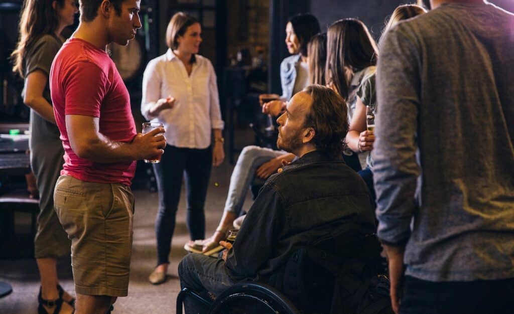 Eine Gruppe von Menschen feiert gemeinsam in entspannter Runde. Eine Person sitzt im Rollstuhl, andere wirken äußerlich nicht betroffen. Das Bild zeigt die Vielfalt im Leben mit Multipler Sklerose und betont, dass jeder Mensch seiner MS einen eigenen Namen geben kann