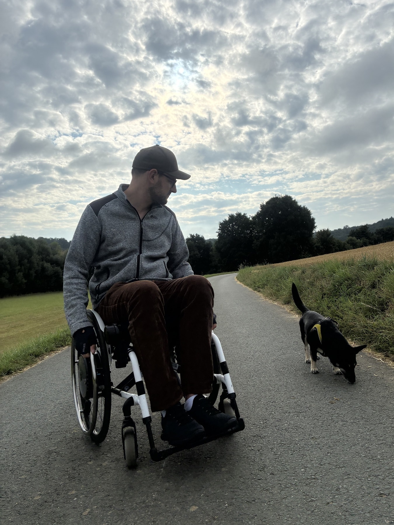 Cedric im Rollstuhl führt seinen Hund auf einer schmalen Landstraße inmitten der Natur aus
