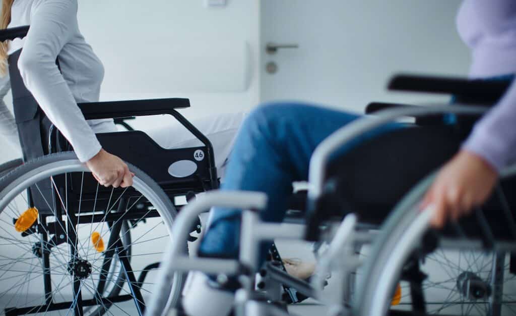 Zwei junge Frauen im Rollstuhl rollen aneinander vorbei in einer Reha-Einrichtung